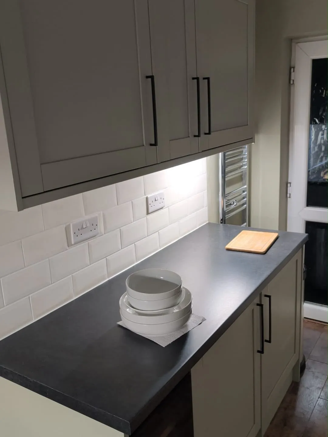 A sage kitchen with under-cabinet lighting and sockets set into the tiles, wired by Harry Radford